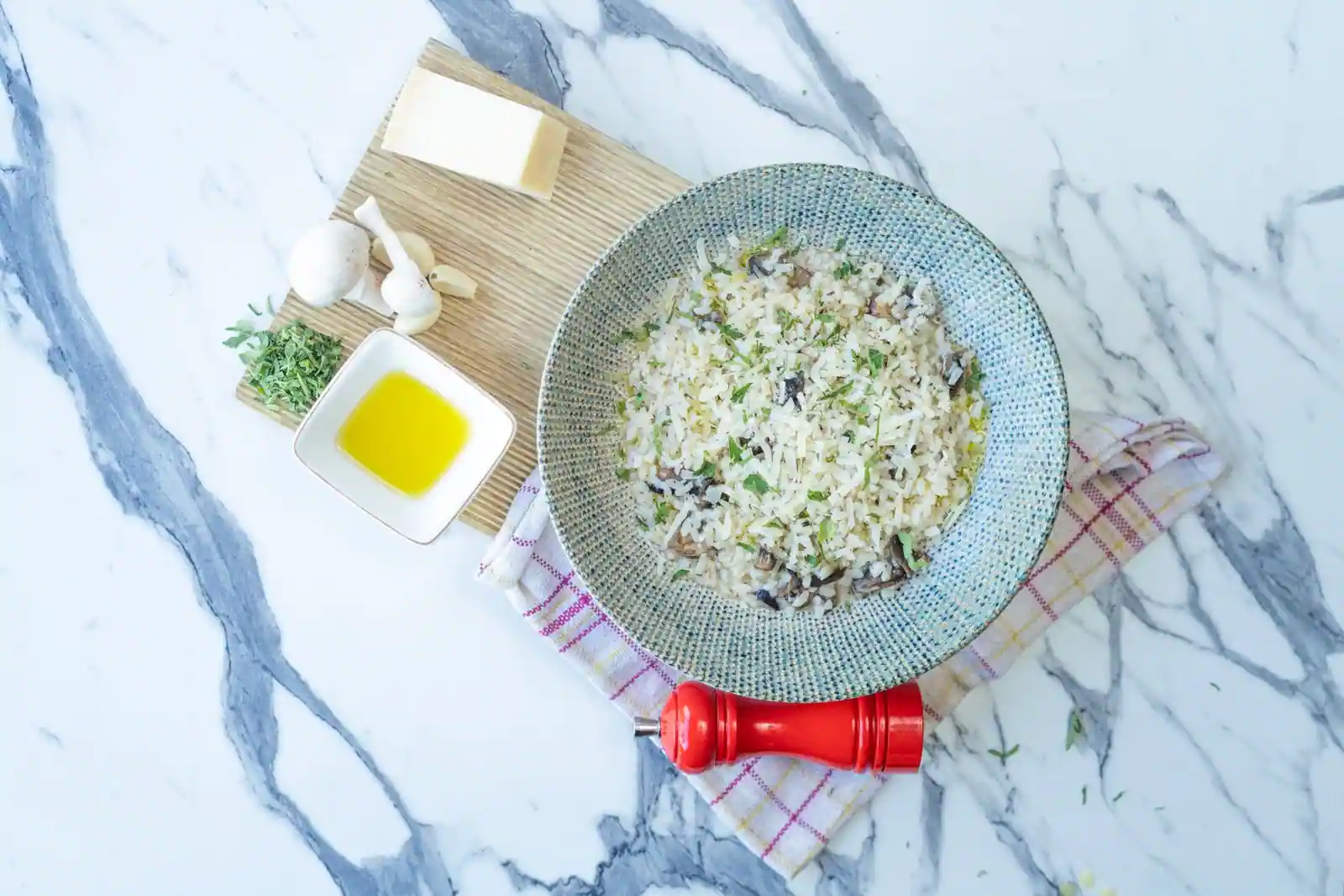 Bol de risotto aux champignons vu de dessus, entouré de parmesan, d'ail et d'herbes sur du marbre