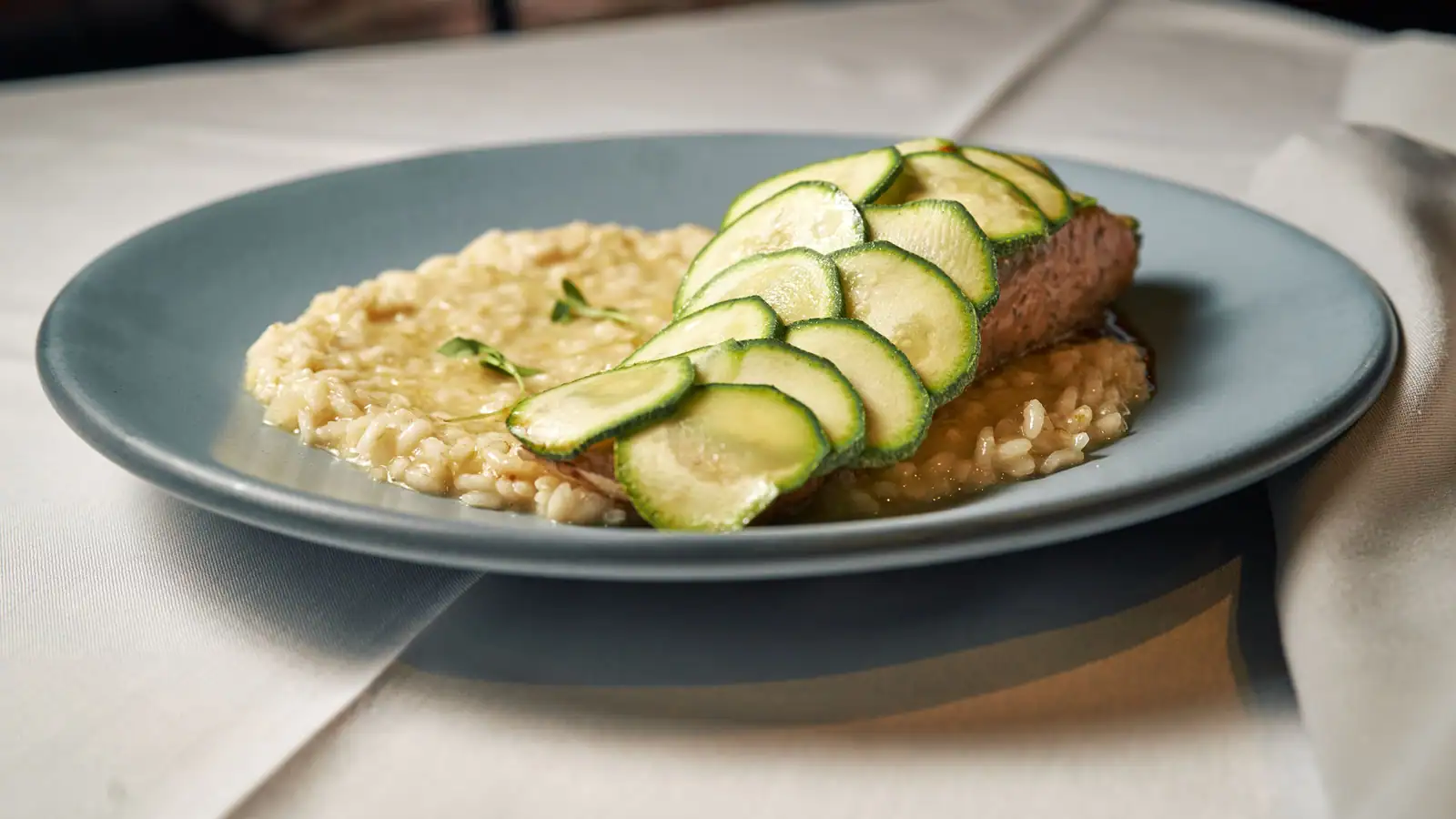 Pavé de saumon recouvert de fines tranches de courgette, posé sur un lit de risotto crémeux