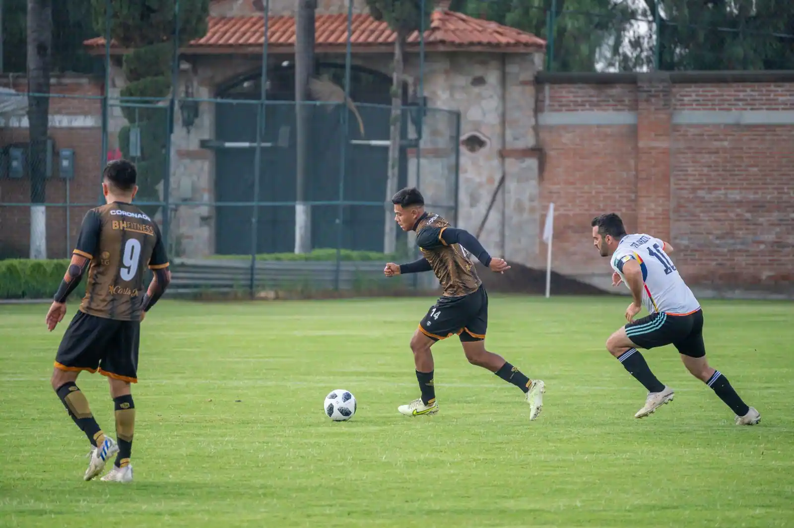 Joueur conduisant le ballon sur une pelouse de football, poursuivi par un adversaire pendant un match
