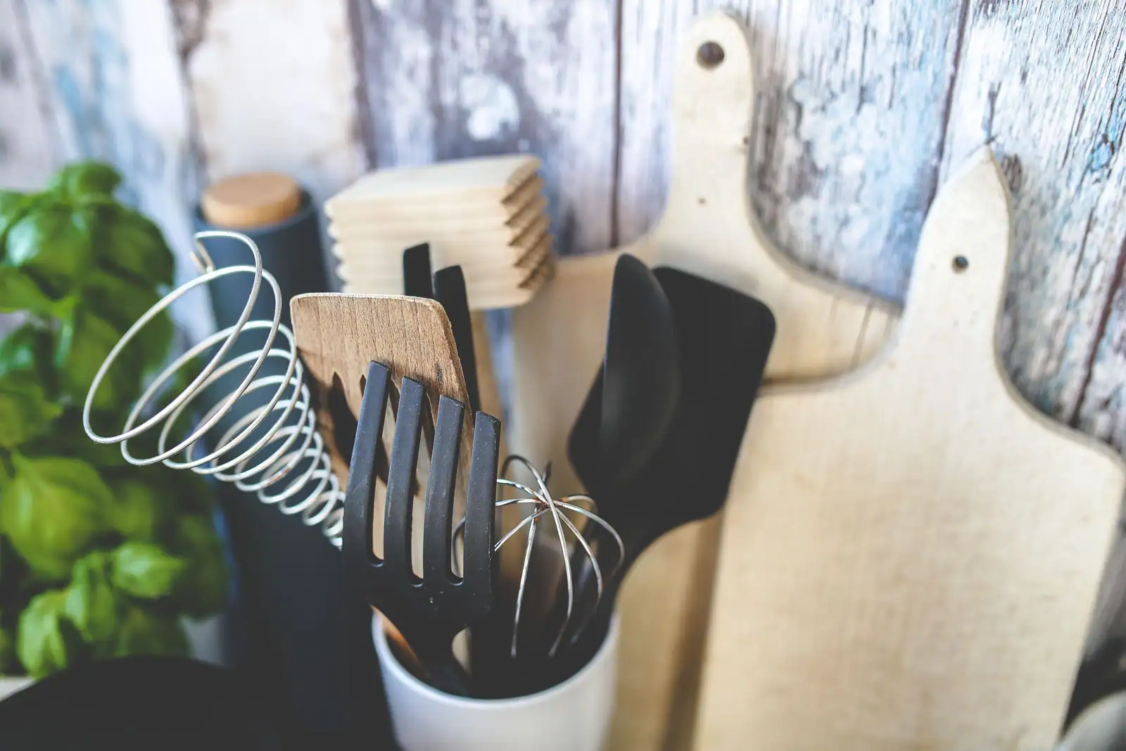 Pot d'ustensiles de cuisine : spatules, fouets et fourchette devant des planches à découper en bois