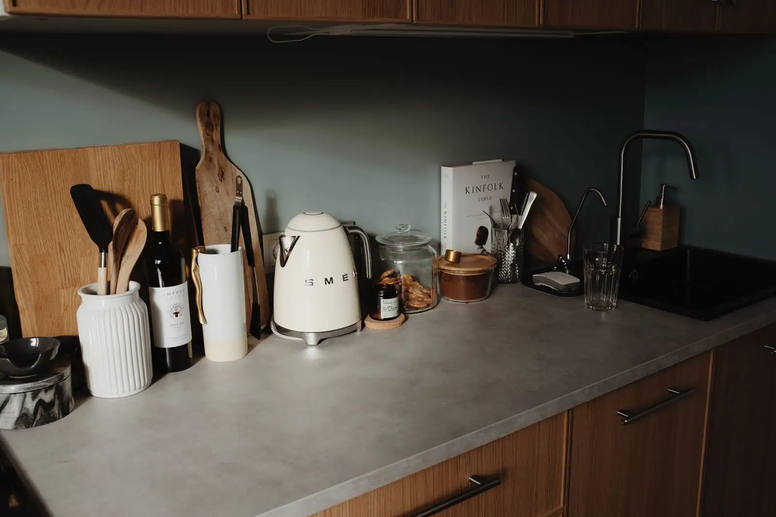 Ustensiles de cuisine en bois dans un pot et planches à découper posés sur un plan de travail.