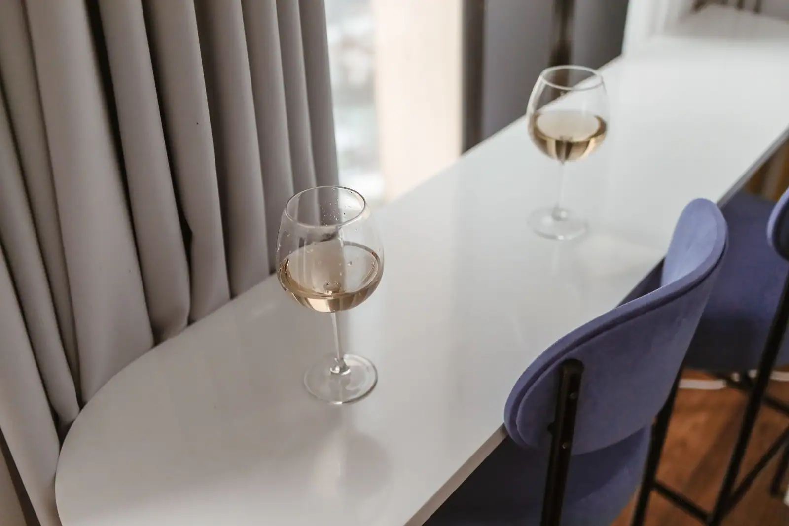 Deux verres de vin blanc servis sur une table blanche, dans une salle claire aux chaises bleues
