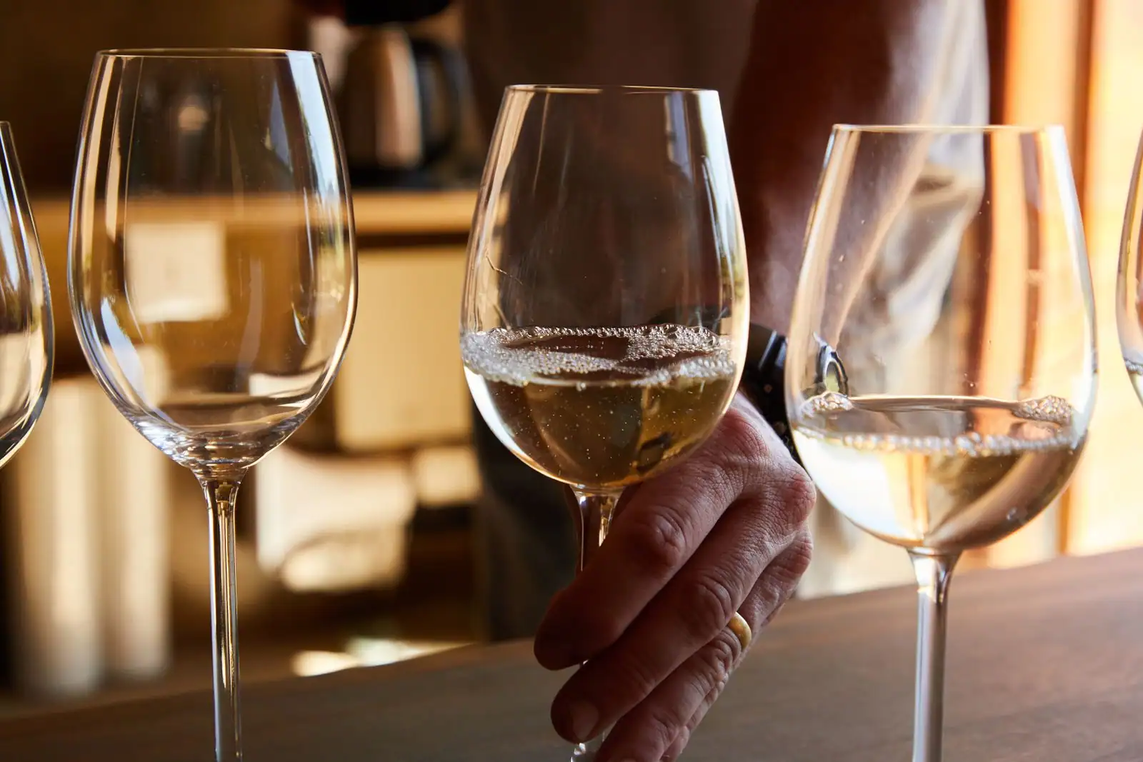 Verres de vin blanc à la robe dorée alignés sur un comptoir lors d'une dégustation en lumière chaude