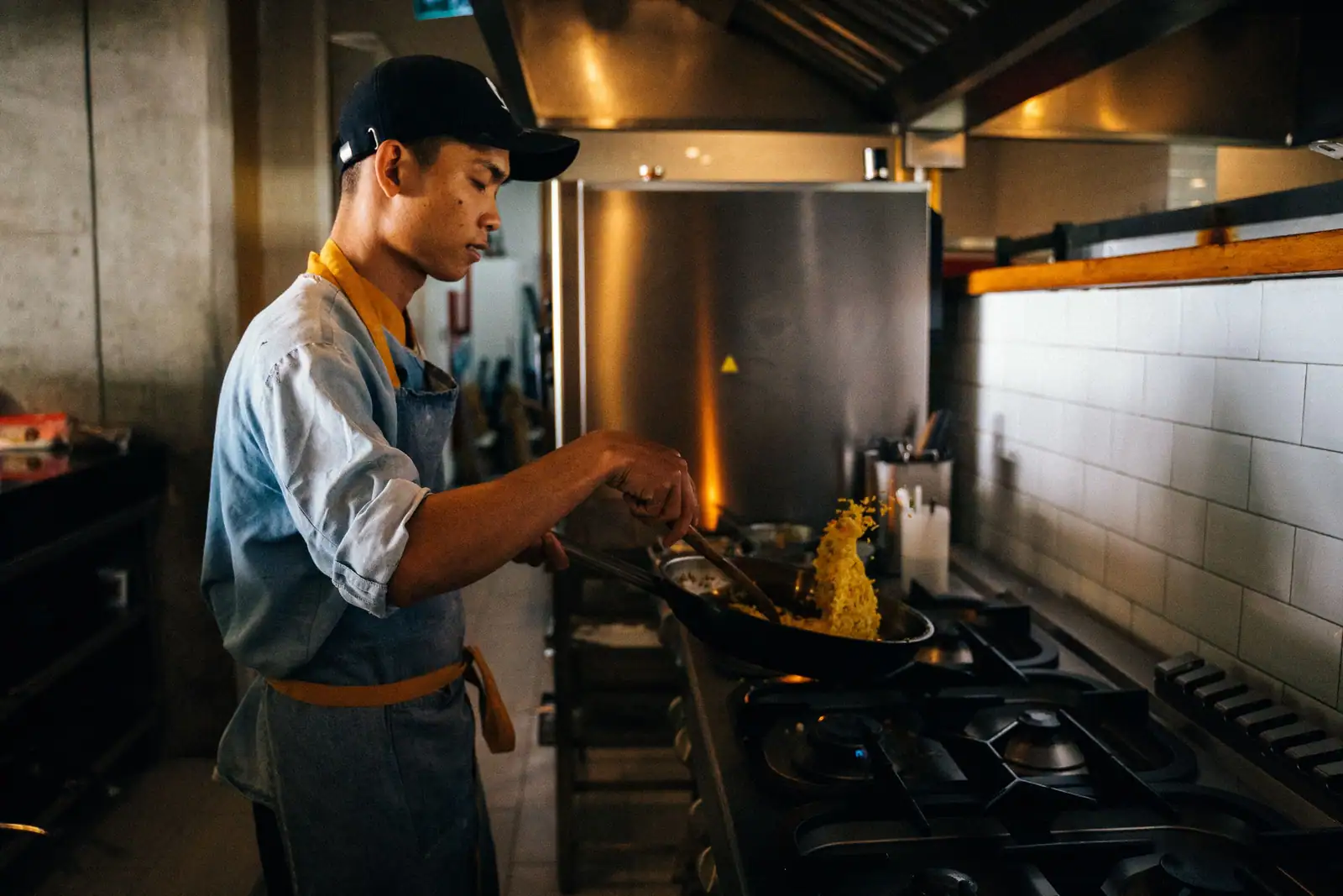 Cuisinier faisant sauter du riz dans un wok sur un fourneau à gaz, en cuisine de restaurant