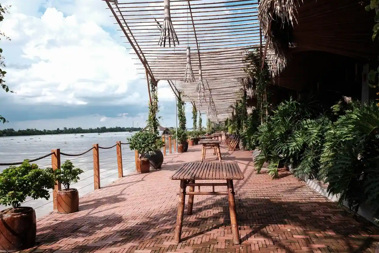 Terrasse de restaurant au bord de l'eau, tables dressées sous des arbres verdoyants