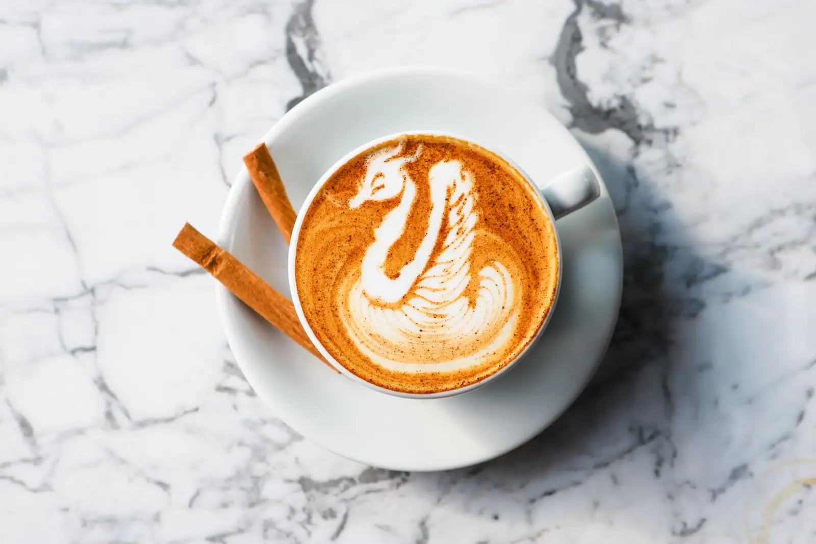Cappuccino avec latte art sur un plan de marbre, accompagné d'un bâton de cannelle