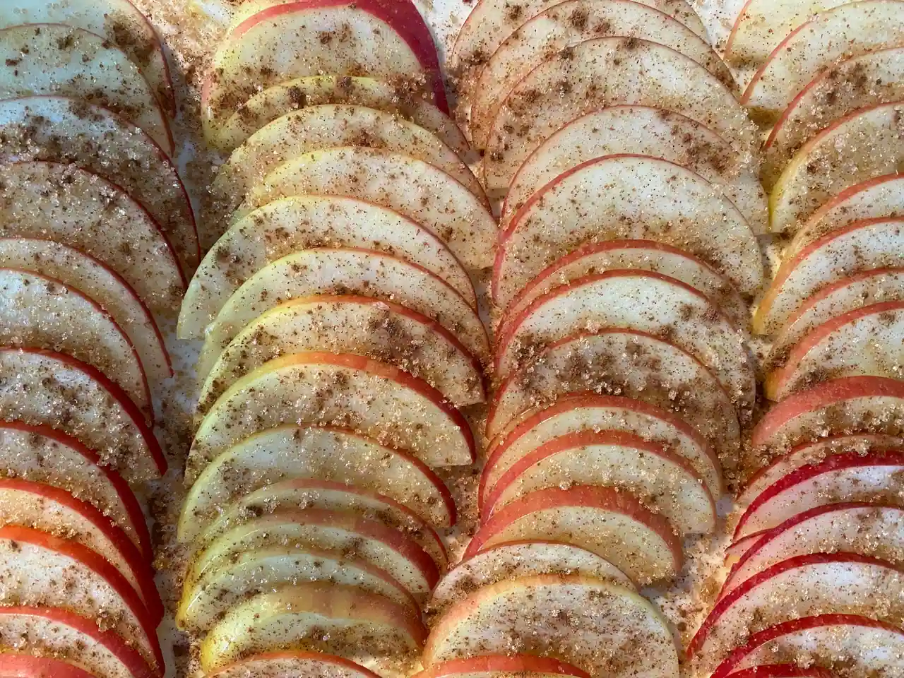 Fines tranches de pomme disposées en rangées, saupoudrées de cannelle et de sucre avant cuisson