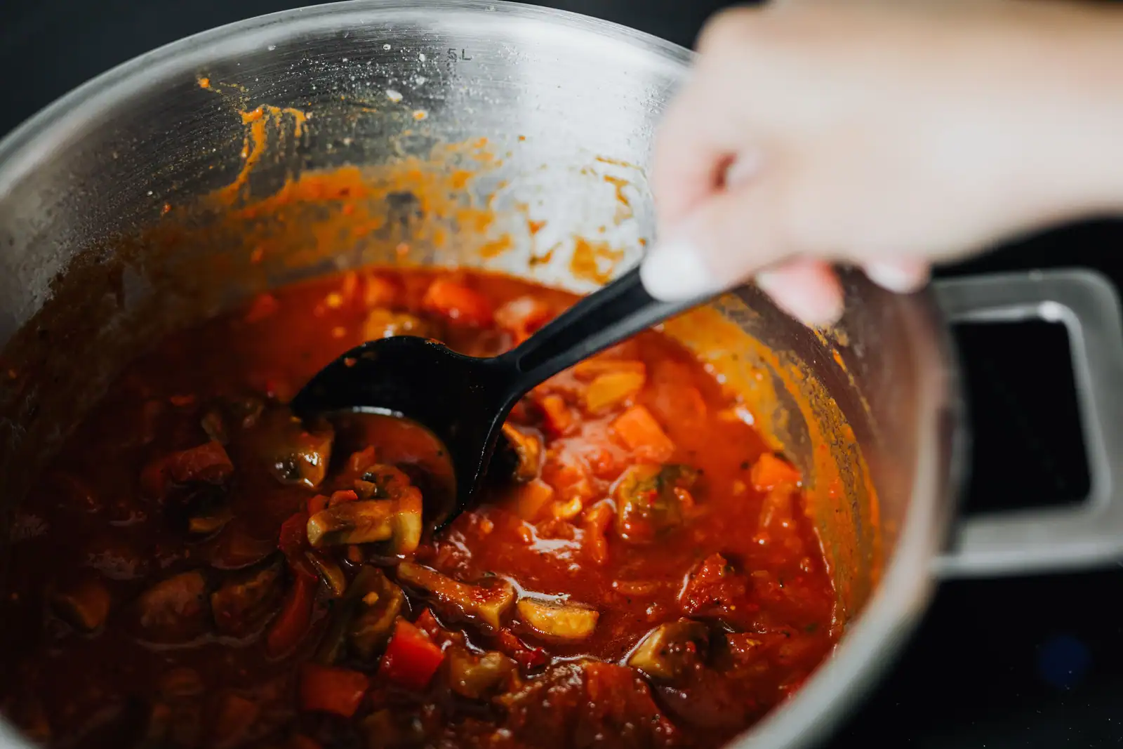 Plat mijoté de légumes d'hiver à la tomate, remué à la cuillère dans une cocotte.